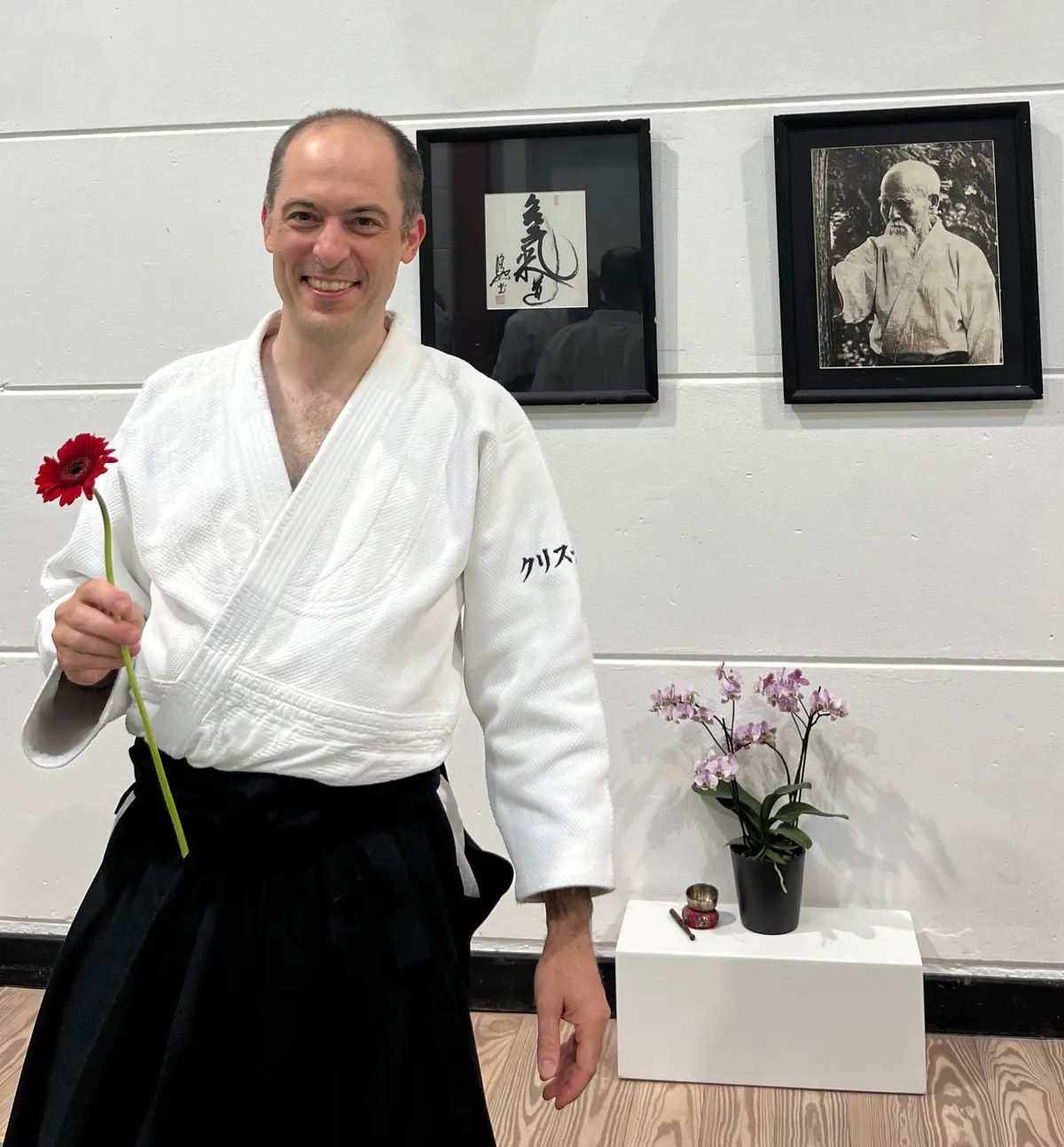 Christian von Baumbach im Aikido-Anzug vor einer Kalligrafie und einem Porträt von Morihei Ueshiba