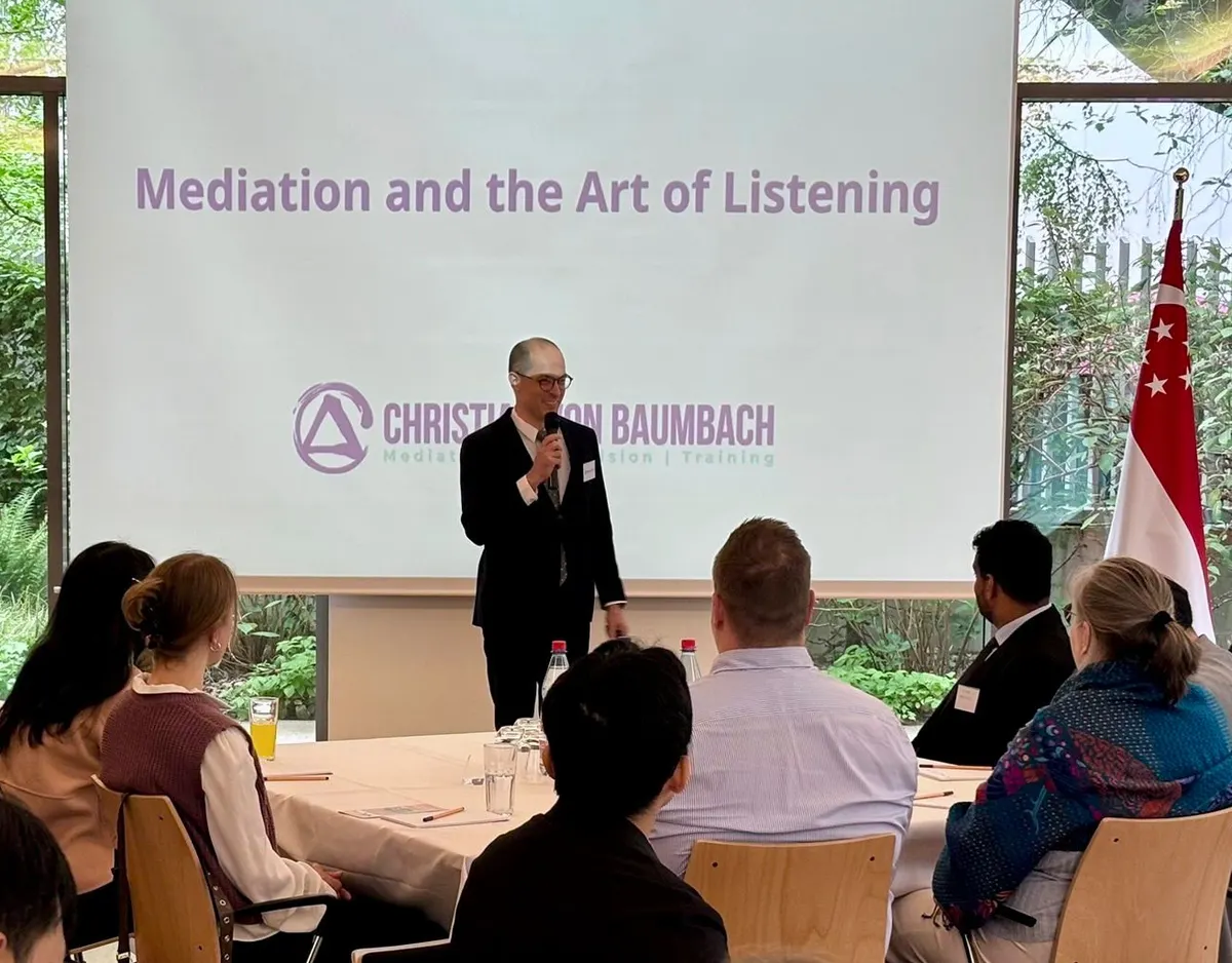 Christian von Baumbach with a microphone in front of the title slide “Mediation and the Art of Listening” at the Singapore Embassy