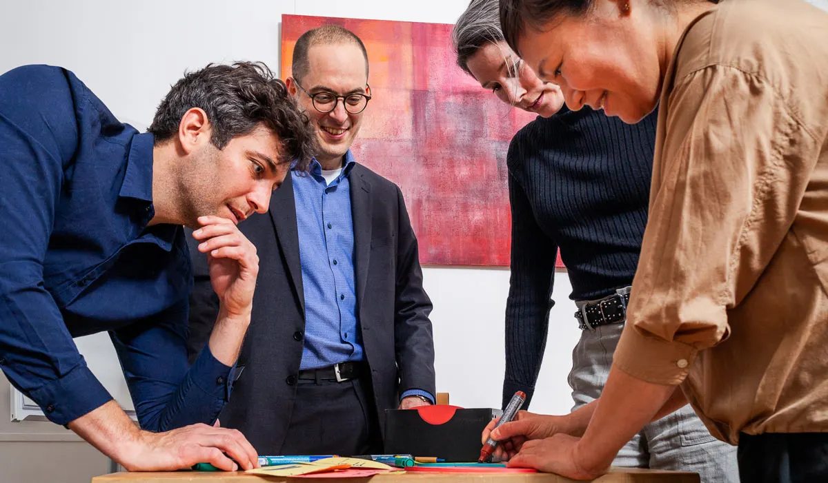 Christian von Baumbach arbeitet mit drei Personen an einem Tisch mit Moderationskarten
